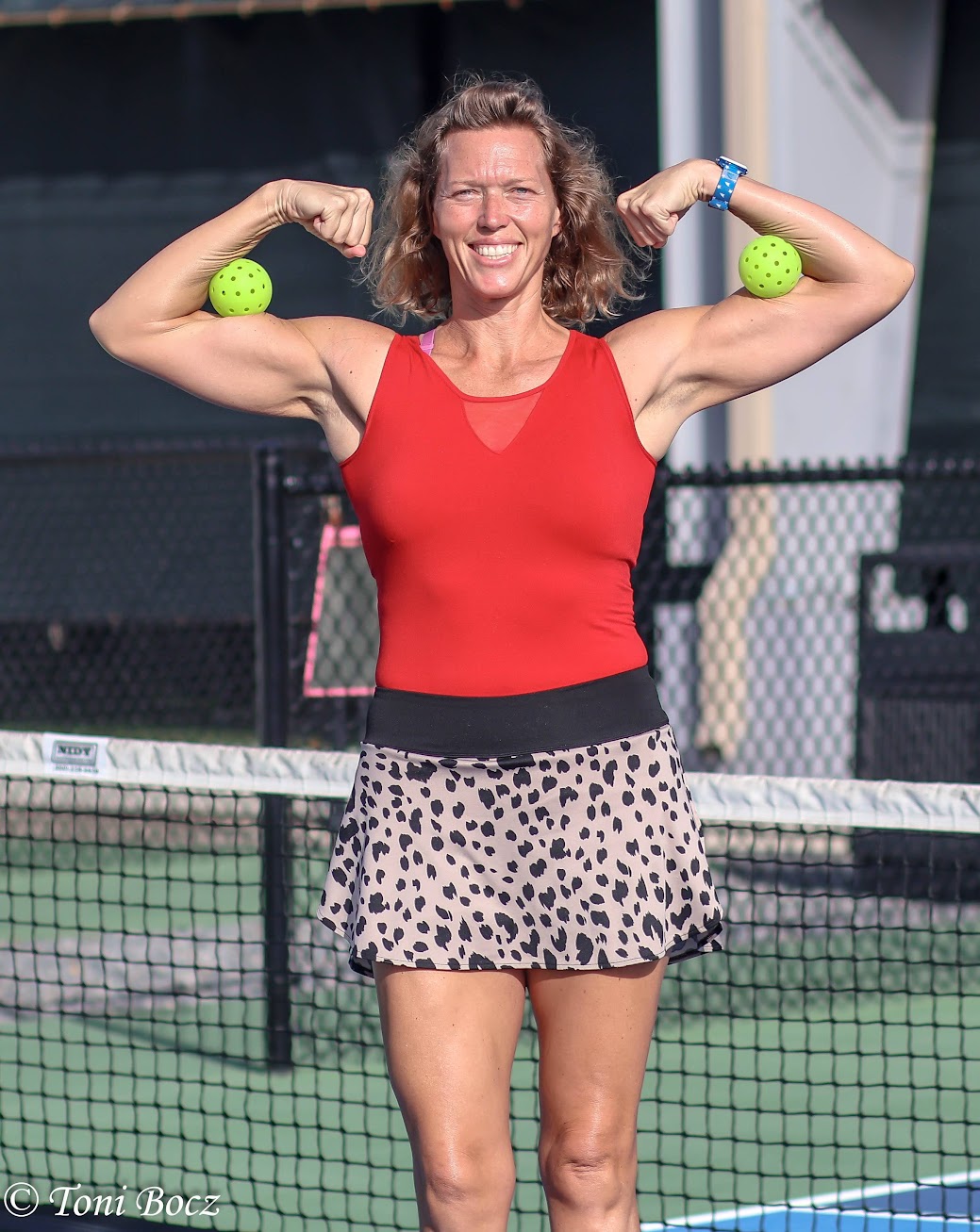 Katy Savage flexing on a pickleball court, holding two pickleballs